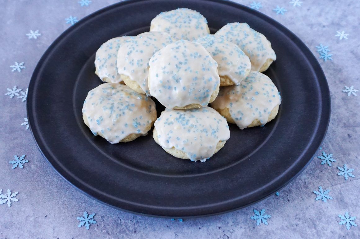 White frosted cookies on a dark plate, with blue sprinkles on a gray cloth background