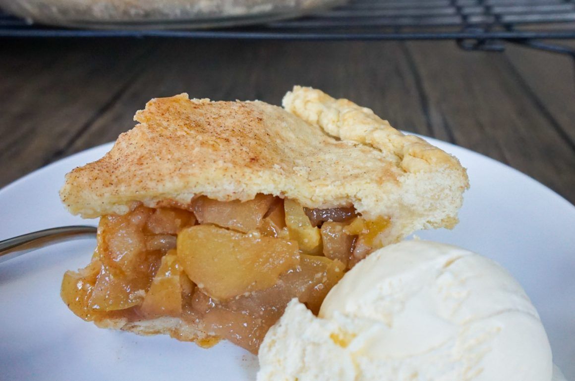 Slice of apple pie with a scoop of vanilla ice cream on a white plate