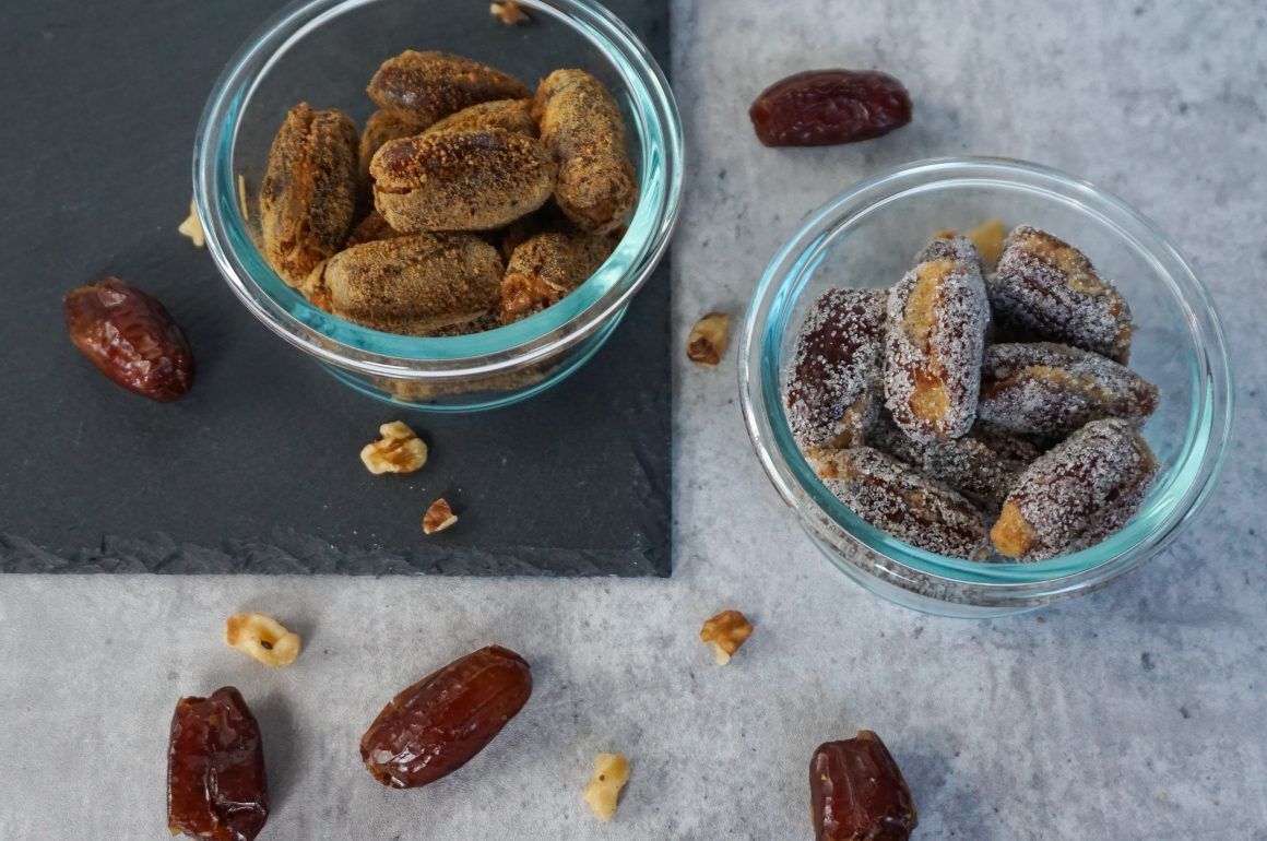 Two glass bowls of date snacks, one sugar-coated, on a gray tabletop with scattered dates.