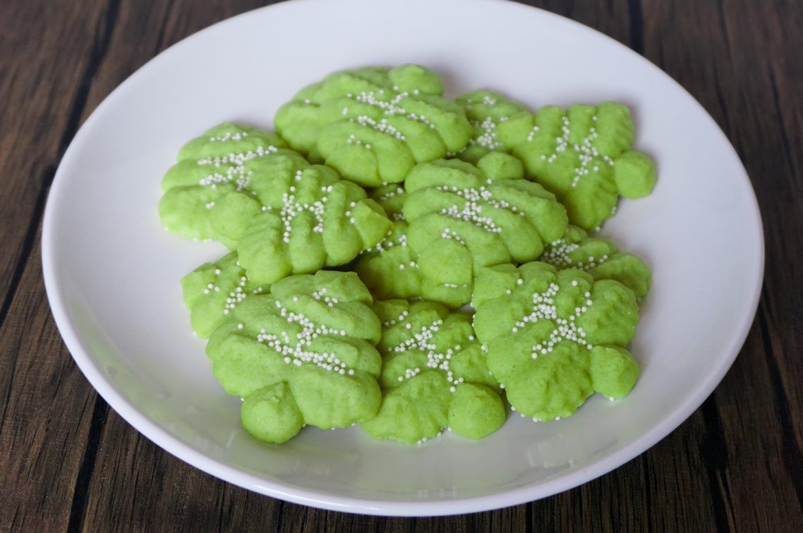 White plate of bright green butterfly-shaped cookies sprinkled with sugar on a dark wooden table