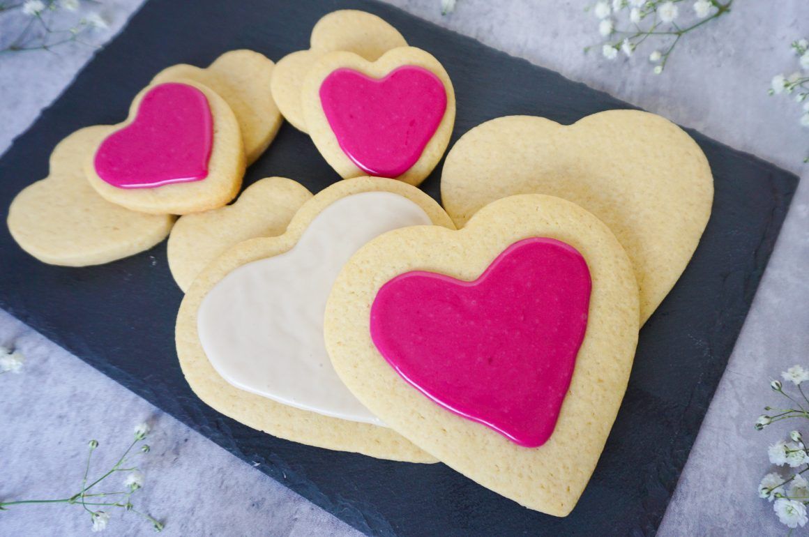 Heart-shaped cookies with pink icing on a dark tray