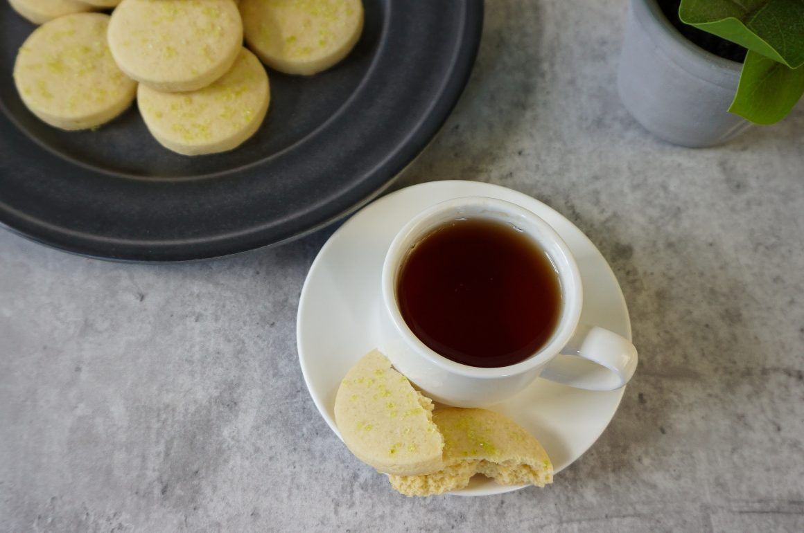 Cup of tea with cookies on a gray tabletop, beside a black plate and a small potted plant