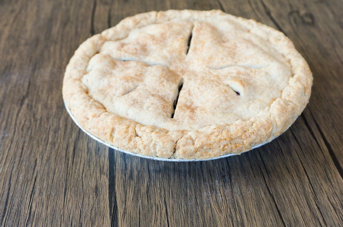 A baked pie in a metal tin on a wooden table, with a golden crust and slits on top