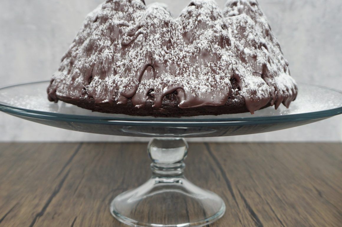Chocolate bundt cake dusted with powdered sugar on a glass pedestal stand