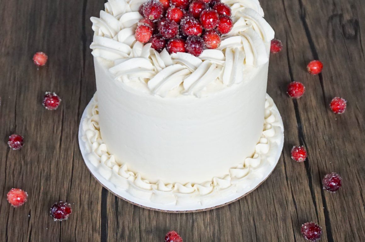 White frosted cake topped with red berries on a rustic wooden table