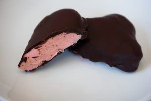 Chocolate-covered candy with a pink filling, one piece cut open on a white surface
