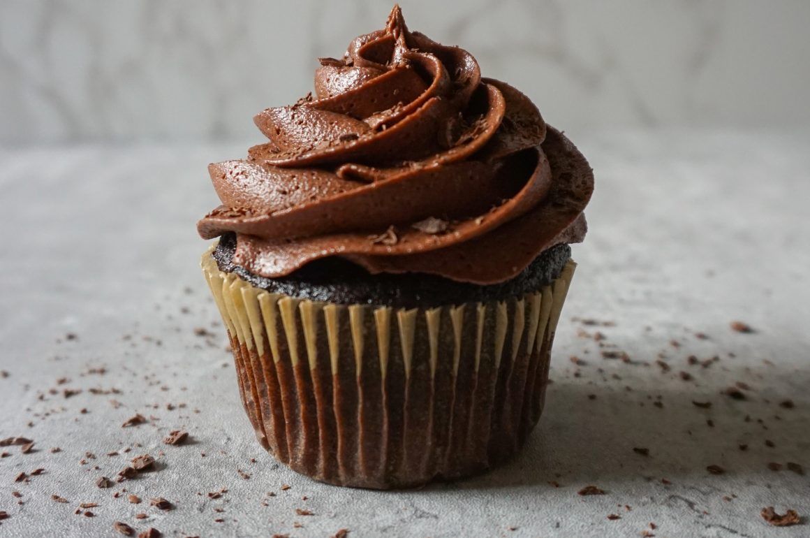 Chocolate cupcake with swirled frosting on a gray surface, sprinkled with cocoa crumbs