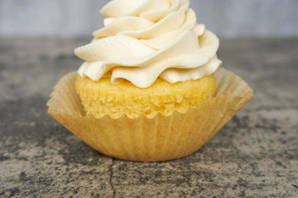Vanilla cupcake with white frosting in a yellow wrapper on a gray surface