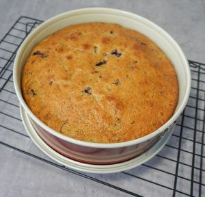 Golden-brown baked cake in a white bowl cooling on a wire rack
