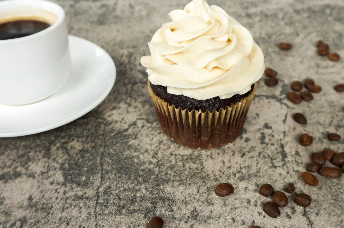 Chocolate cupcake with white frosting beside a cup of coffee on a rustic surface