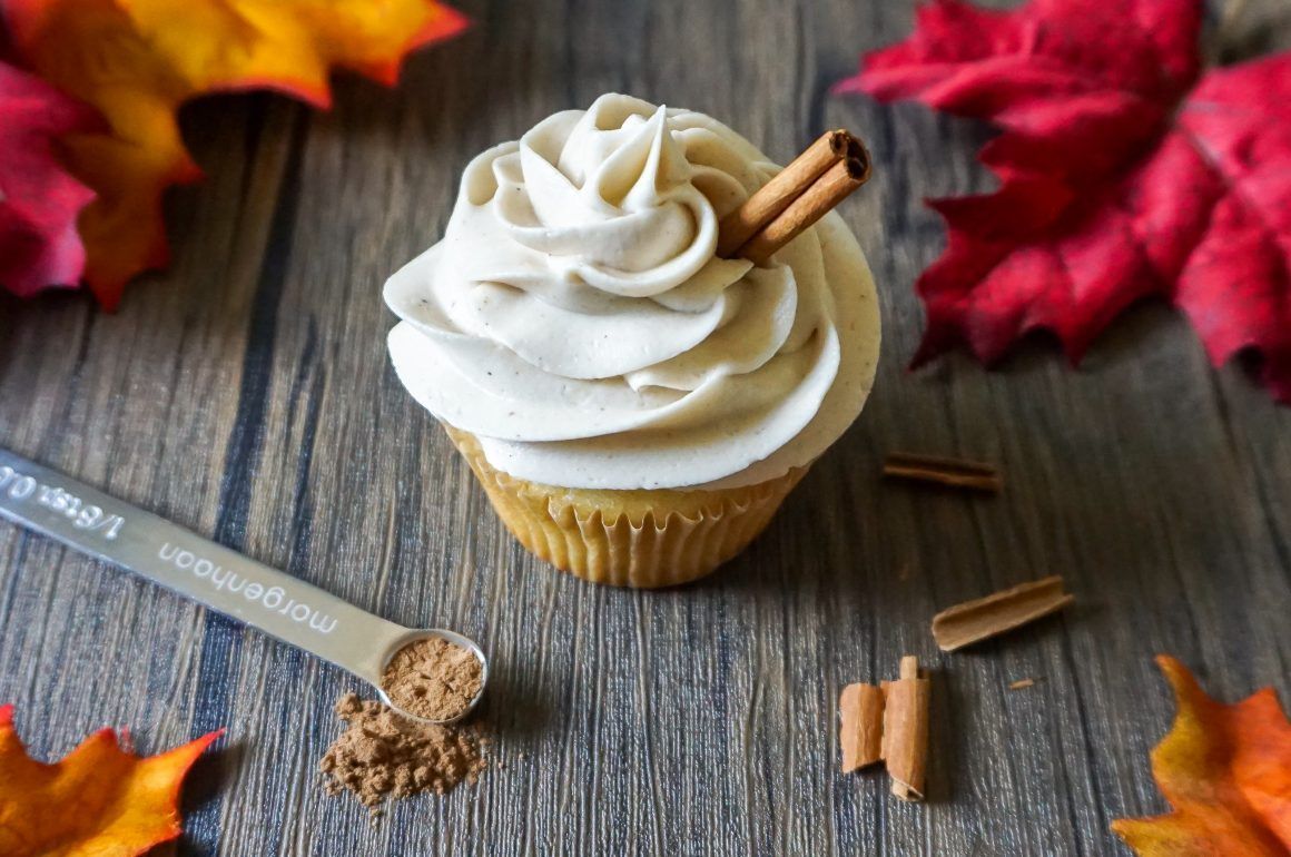 Cupcake with white frosting and cinnamon sticks on a rustic wooden table with fall leaves
