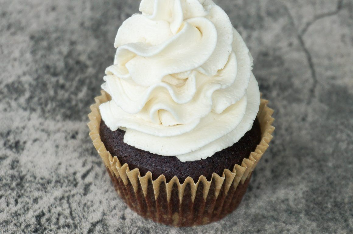 Chocolate cupcake with white swirled frosting on a gray stone surface
