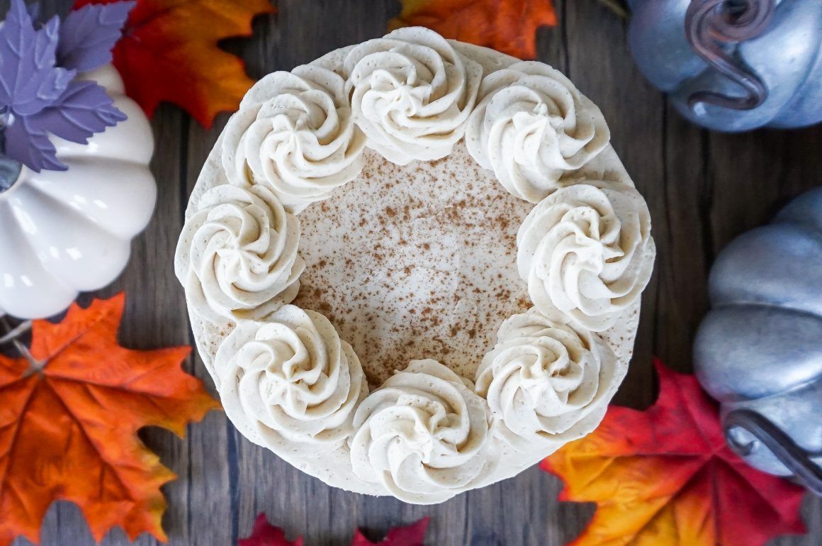 White frosted cake with rosette border on a dark table, surrounded by autumn leaves and berries