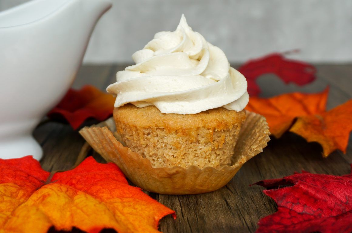 Cupcake with white frosting on a wooden table, surrounded by red and orange autumn leaves