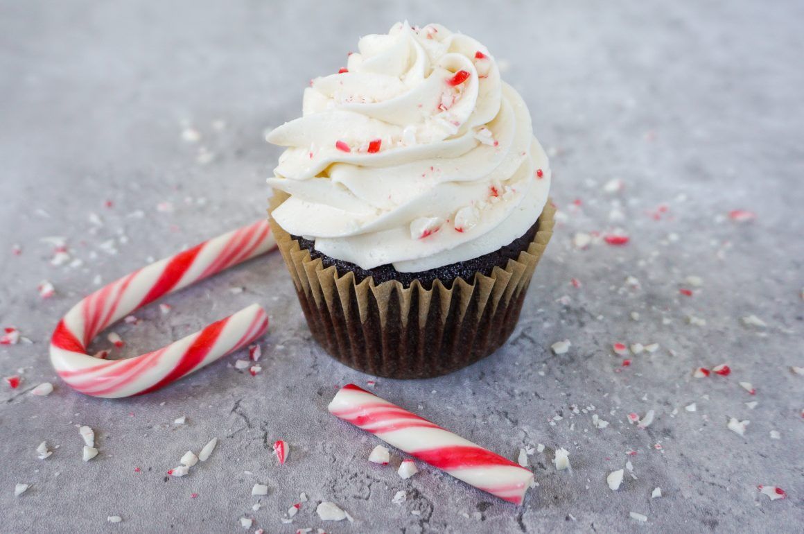 Chocolate cupcake with white frosting and red sprinkles beside red-and-white candy canes on a gray surface