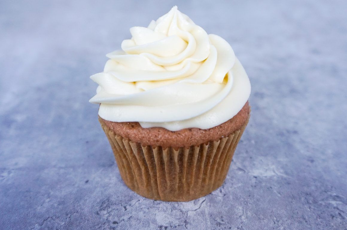 White frosted cupcake in a brown wrapper on a blue background