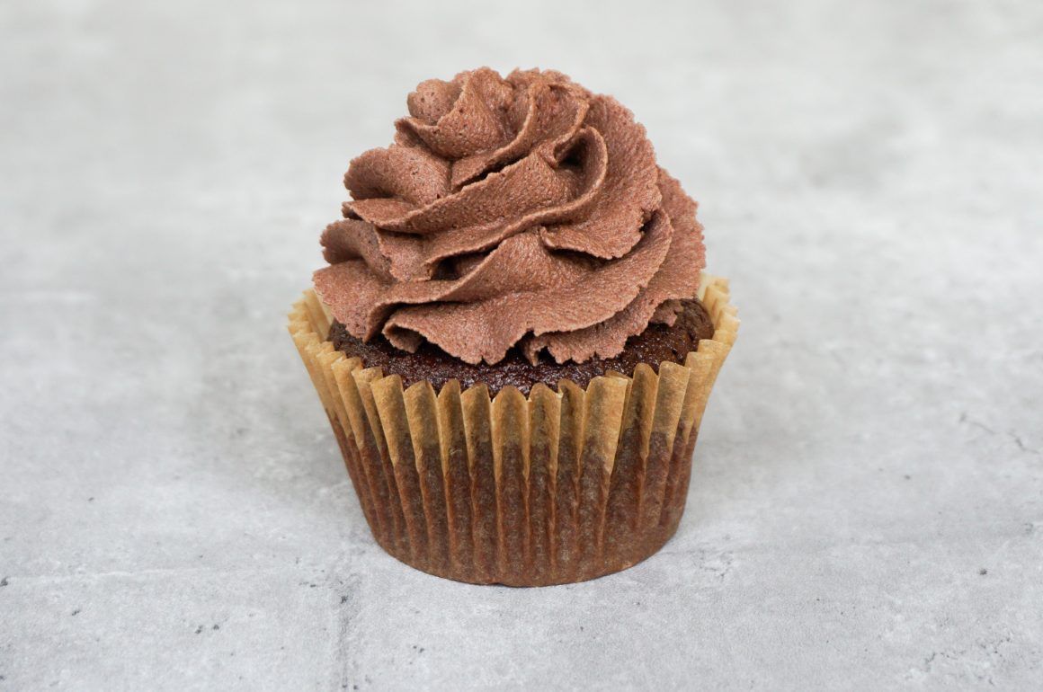 Chocolate cupcake with swirled chocolate frosting on a light gray surface