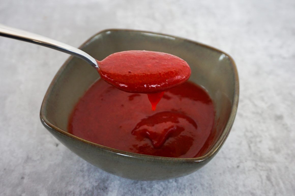 Spoonful of red sauce over a bowl of red sauce on a gray surface