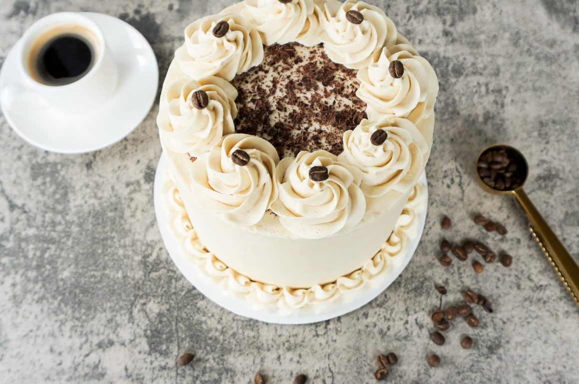 White frosted cake with chocolate garnish beside a coffee cup and spoon on a gray surface