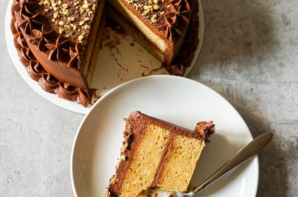Slice of yellow layer cake on a plate beside the remaining chocolate-frosted cake, with a serving knife