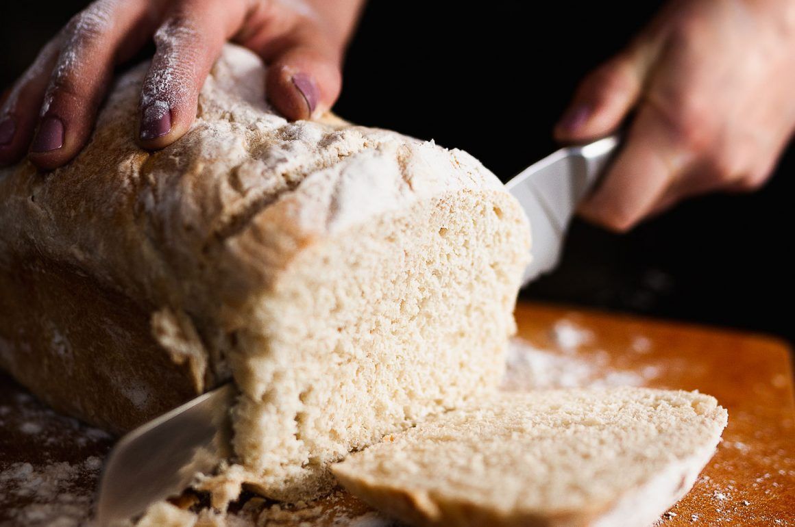 Hands slicing a loaf of bread on a wooden board