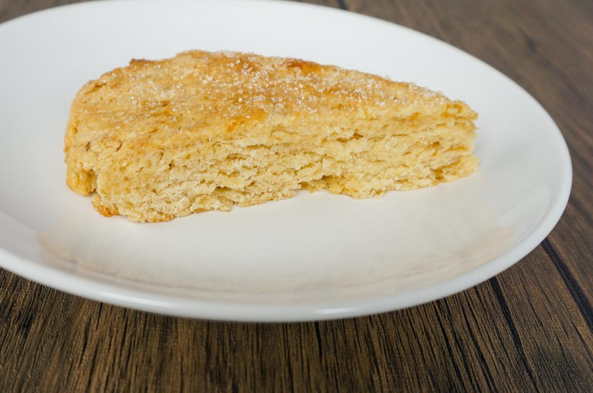 Slice of golden scone on a white plate against a wooden table