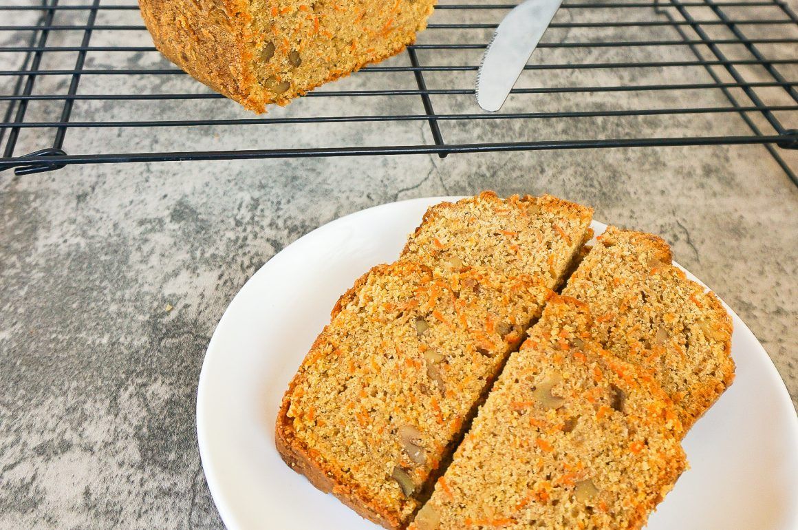 Two slices of orange-speckled loaf on a white plate, with more cooling on a wire rack behind.
