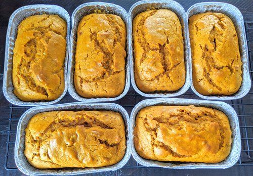 Seven loaf pans filled with baked golden-orange batter, arranged in two rows on a baking tray.