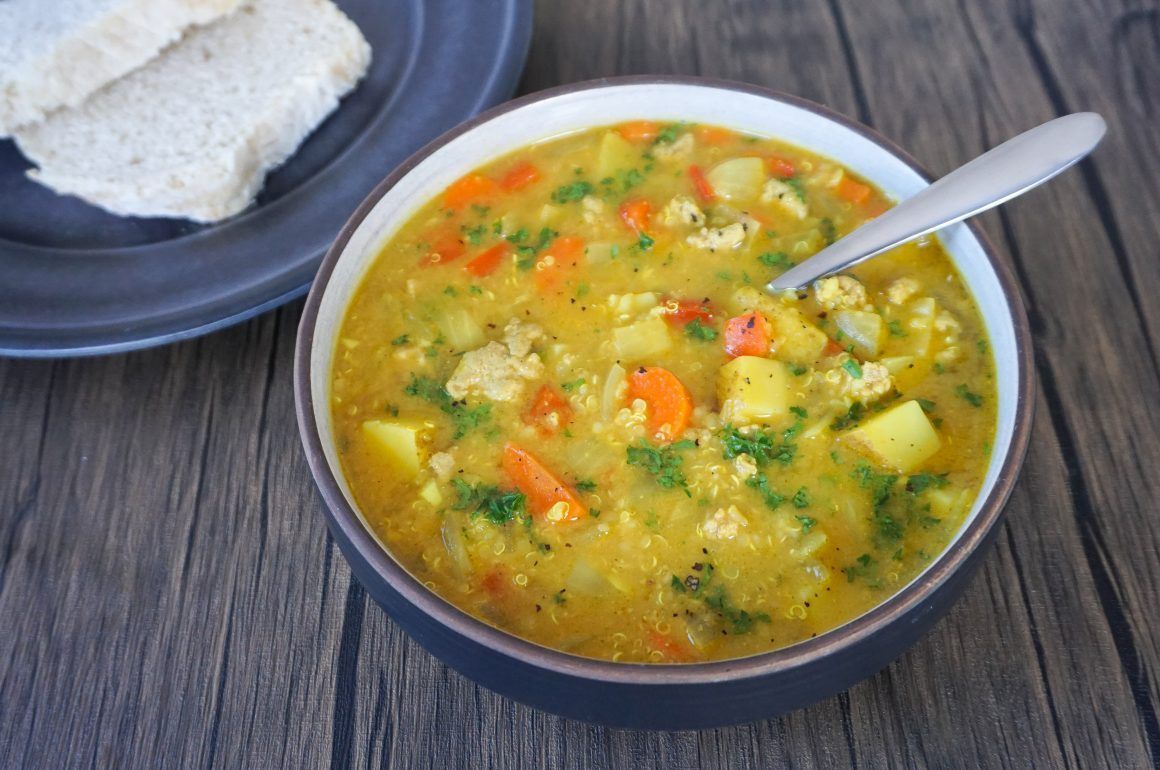 Bowl of vegetable soup with a spoon, served beside a piece of bread on a dark wooden table.