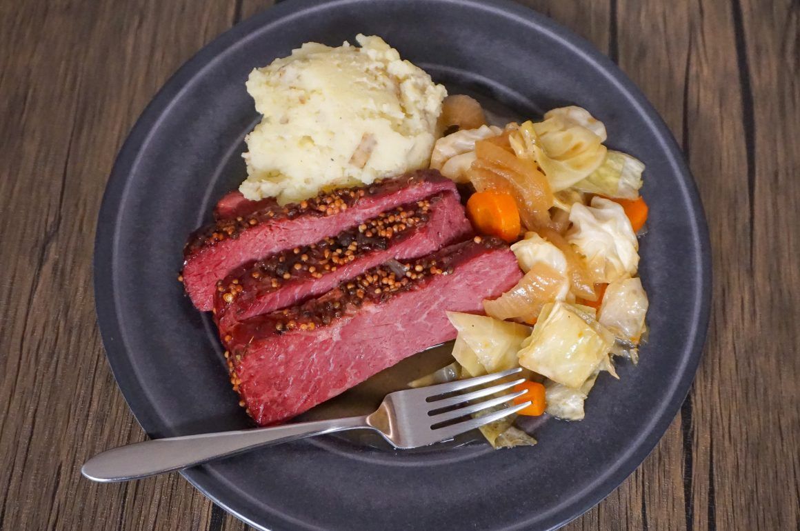 Plate with sliced steak, mashed potatoes, and mixed vegetables on a wooden table with a fork.