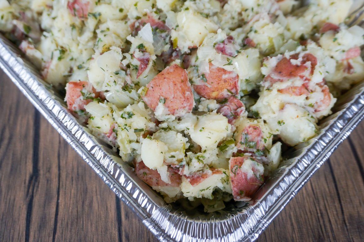 Foil tray of mixed potato casserole with diced red sausage and green herbs