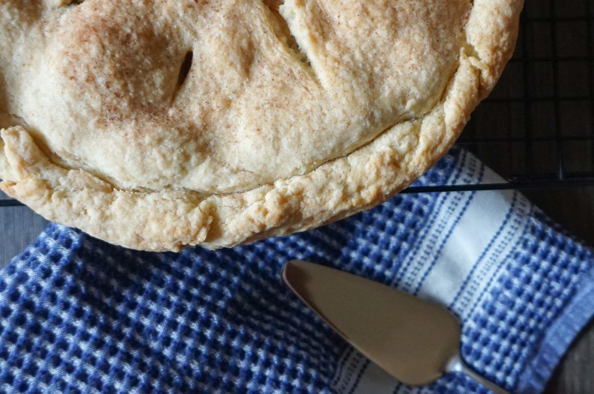 A golden-brown pie on a blue checkered cloth beside a pie server.