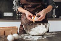 Person cracking an egg into a bowl of flour while baking in a kitchen