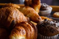 Assorted croissants, muffins, and pastries displayed on a bakery tray