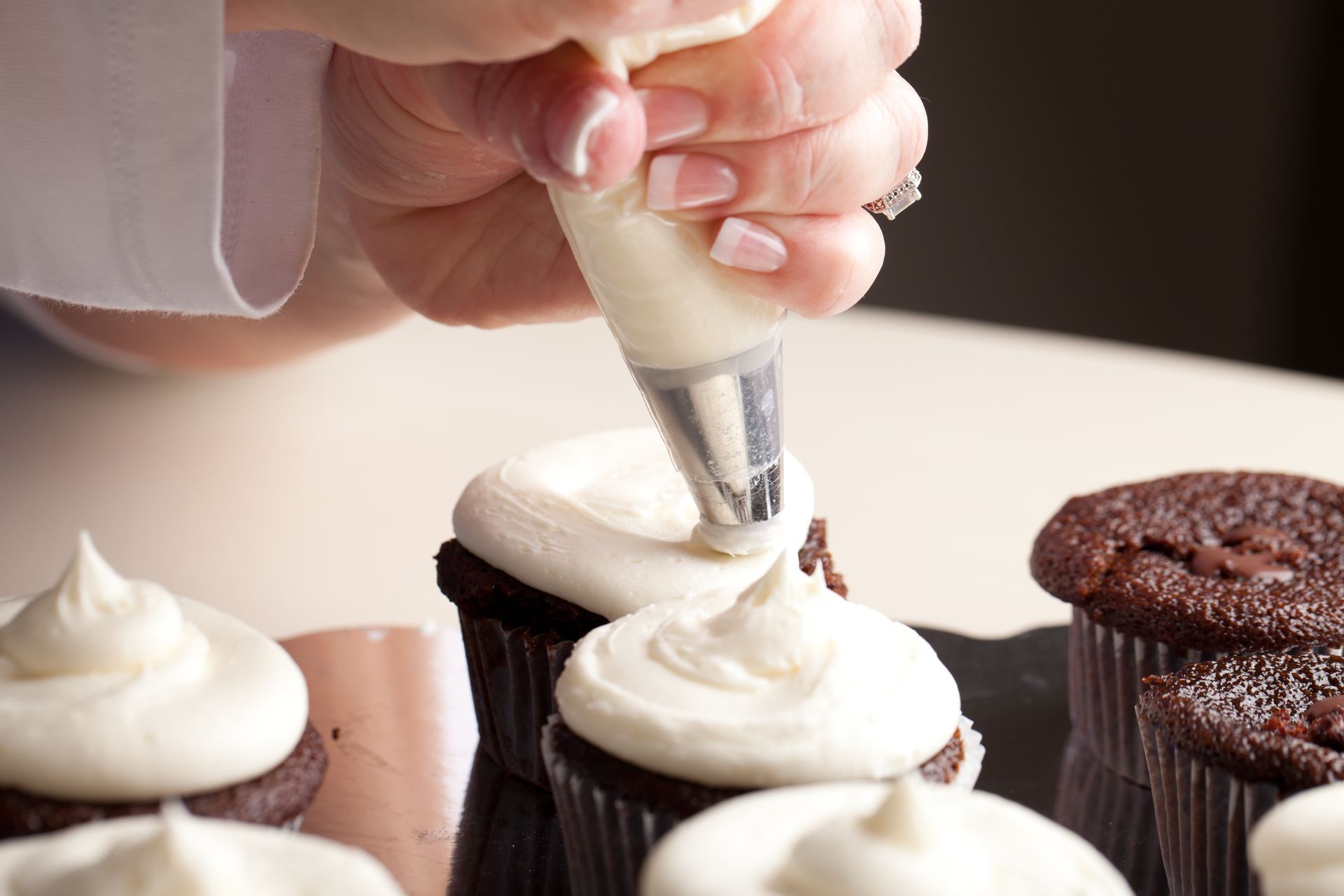 Hand piping white frosting onto chocolate cupcakes on a tray