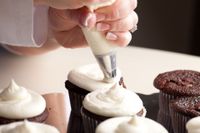 Hand piping white frosting onto chocolate cupcakes on a tray