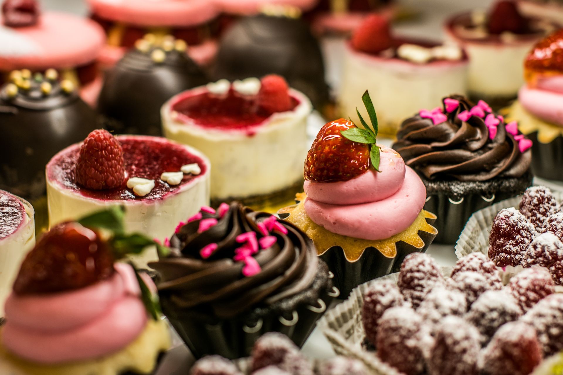 Assorted decorated cupcakes with pink, chocolate, and powdered toppings, arranged on a dessert tray