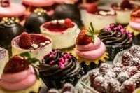 Assorted decorated cupcakes with pink, chocolate, and powdered toppings, arranged on a dessert tray