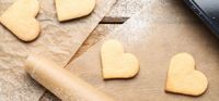 Heart-shaped cookies on parchment paper with a rolling pin and dusted flour.