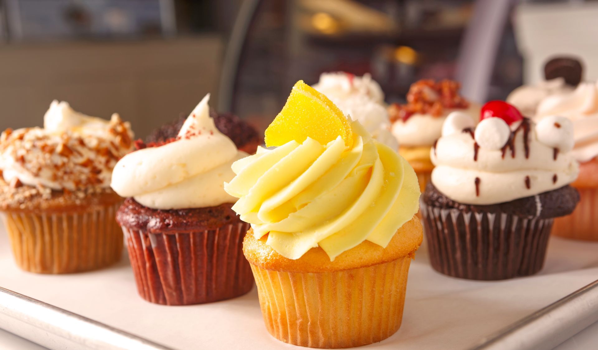 Assorted frosted cupcakes on a tray, including yellow, white, and chocolate-topped varieties.