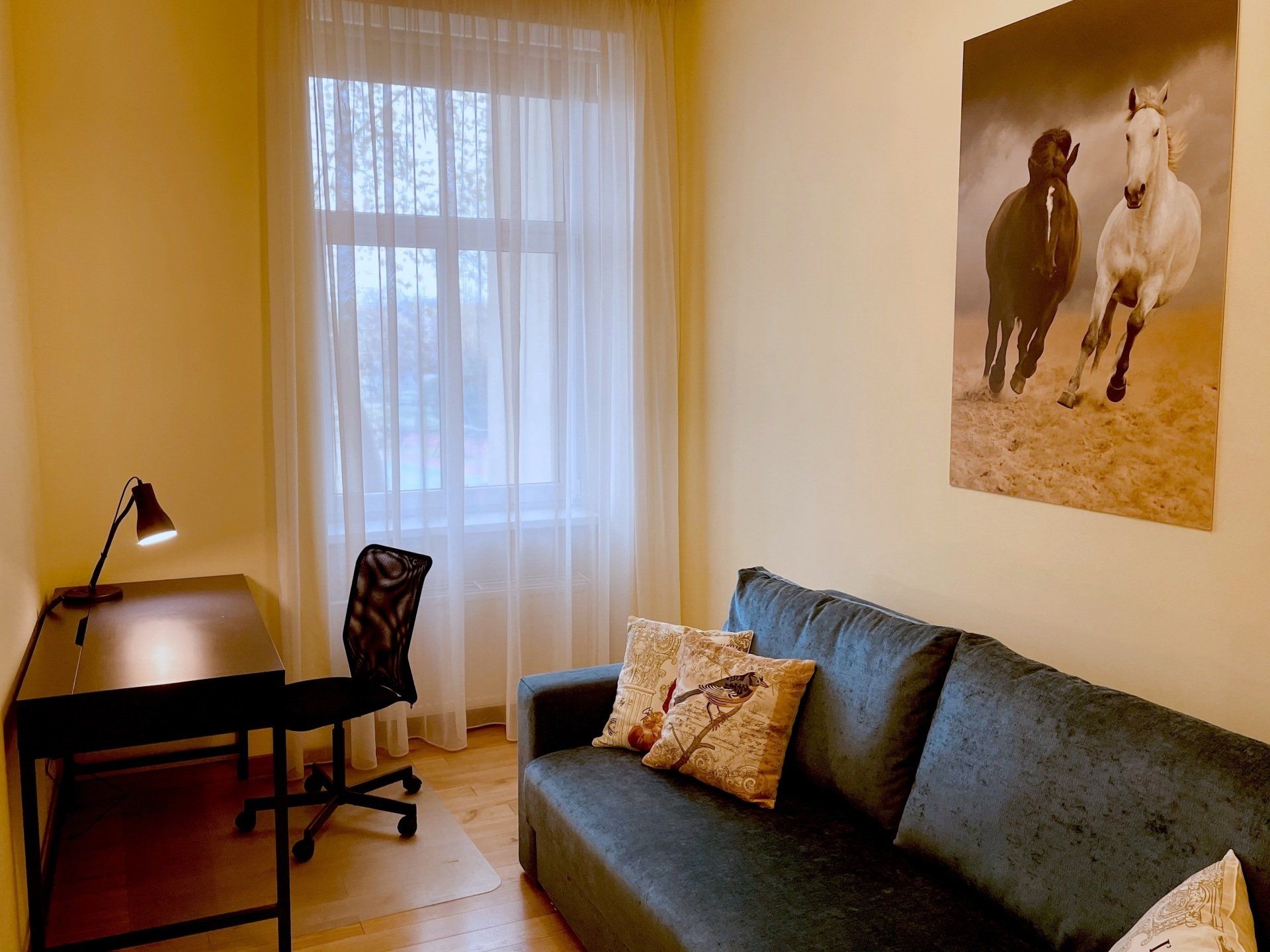 A living room with a couch a desk and a picture of horses on the wall