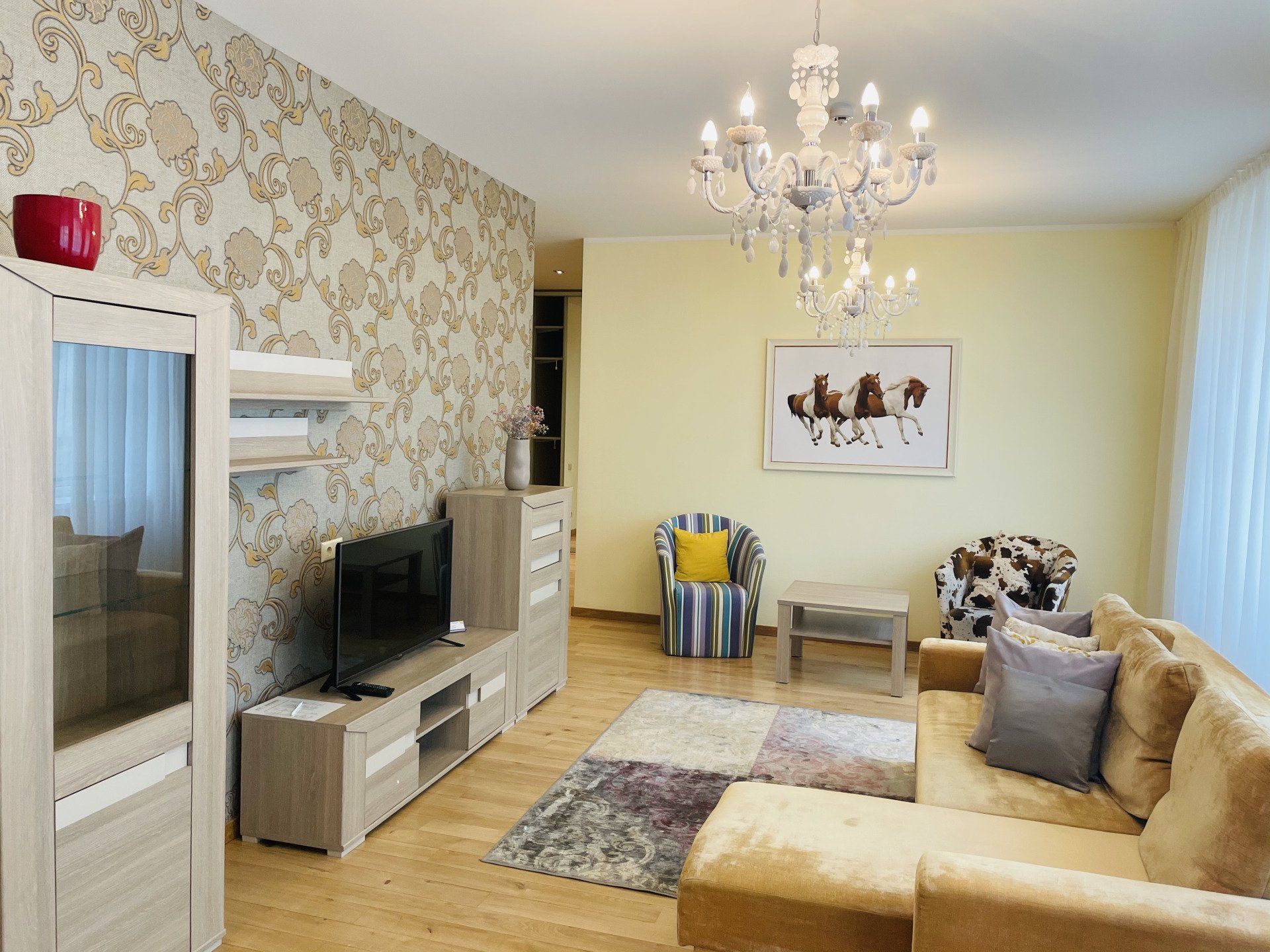 A living room with a couch , chair , television and chandelier.