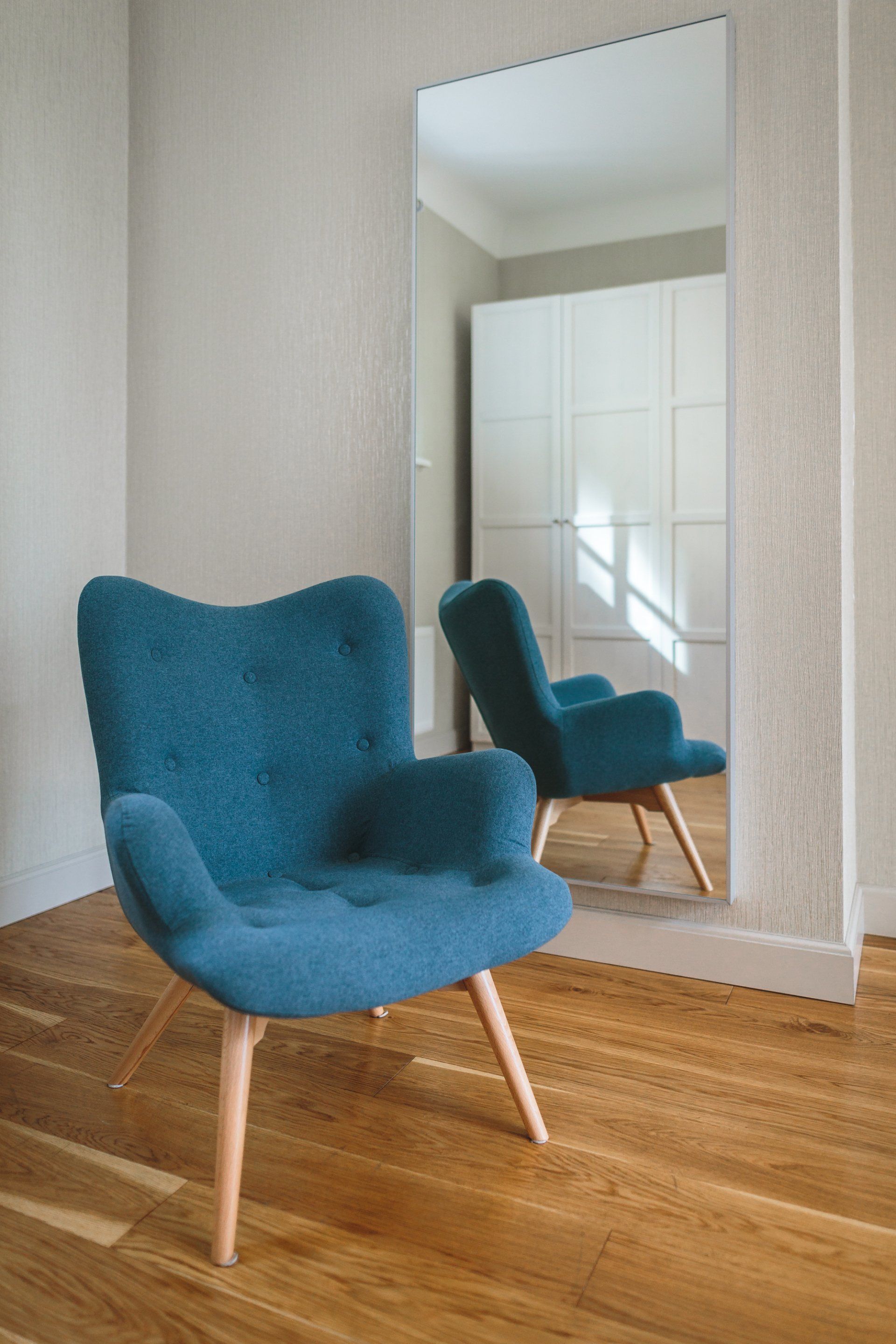 A blue chair is sitting in front of a large mirror in a room.