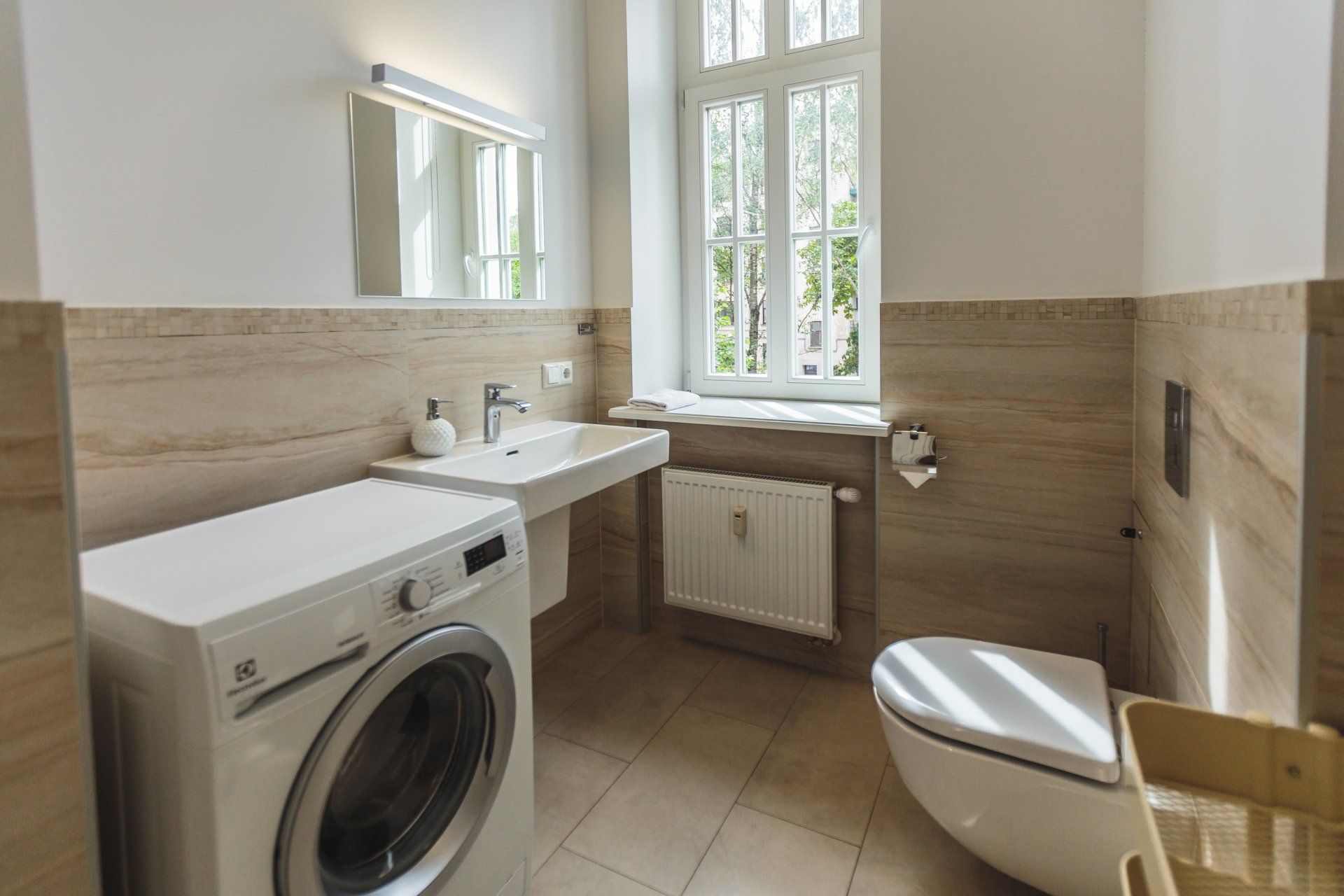 A bathroom with a washing machine , toilet , sink and mirror.