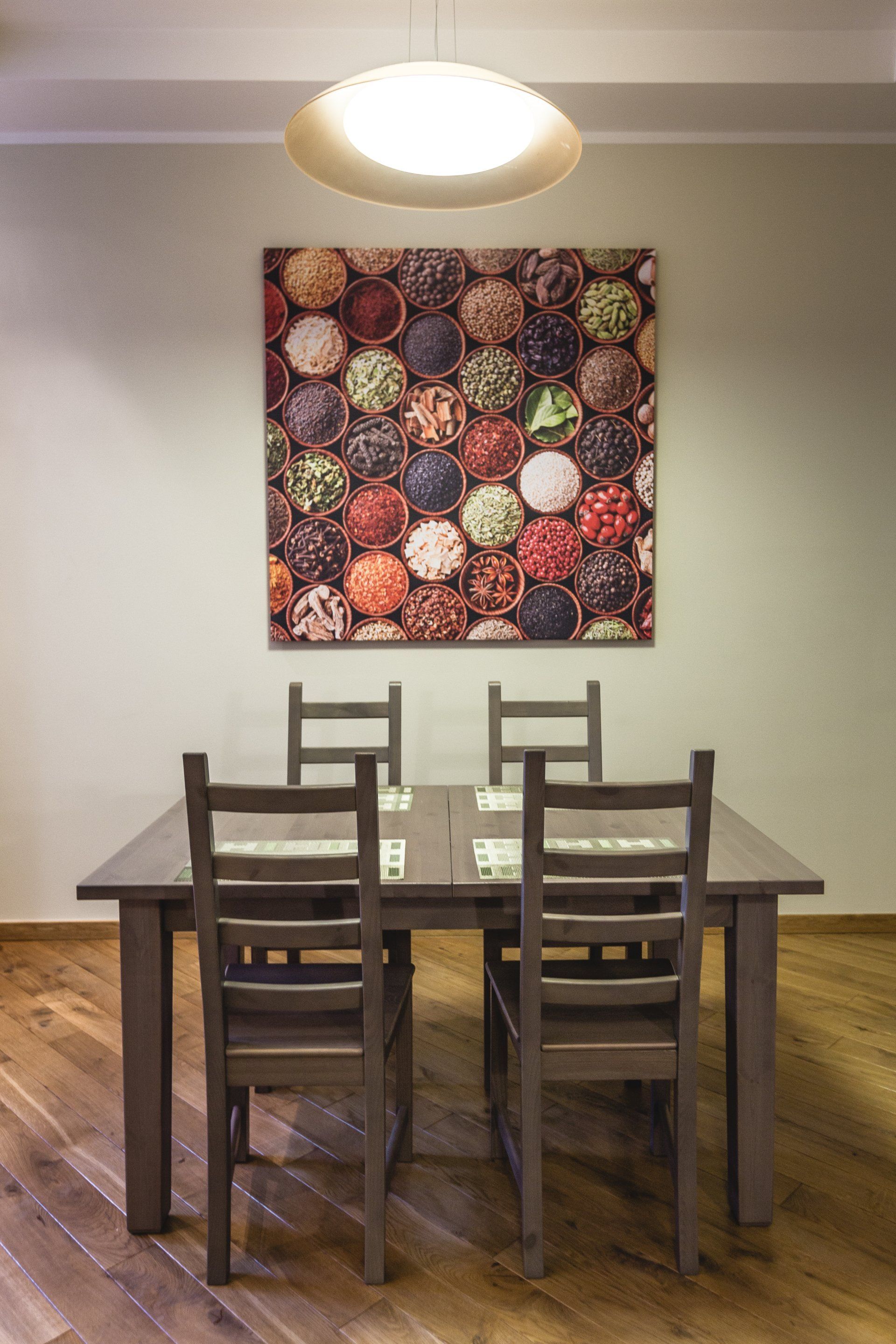A dining room with a table and chairs and a painting of spices on the wall.