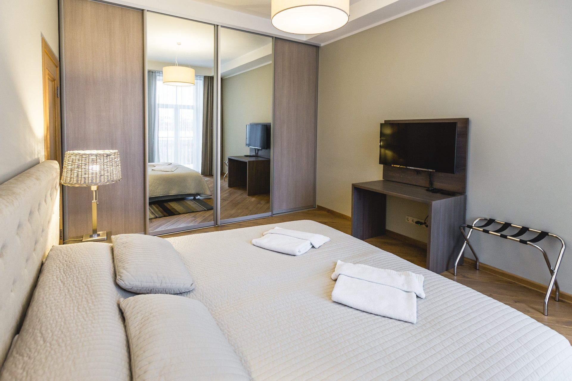 A bedroom with a king size bed , sliding mirrored wardrobes , a flat screen tv and a desk.