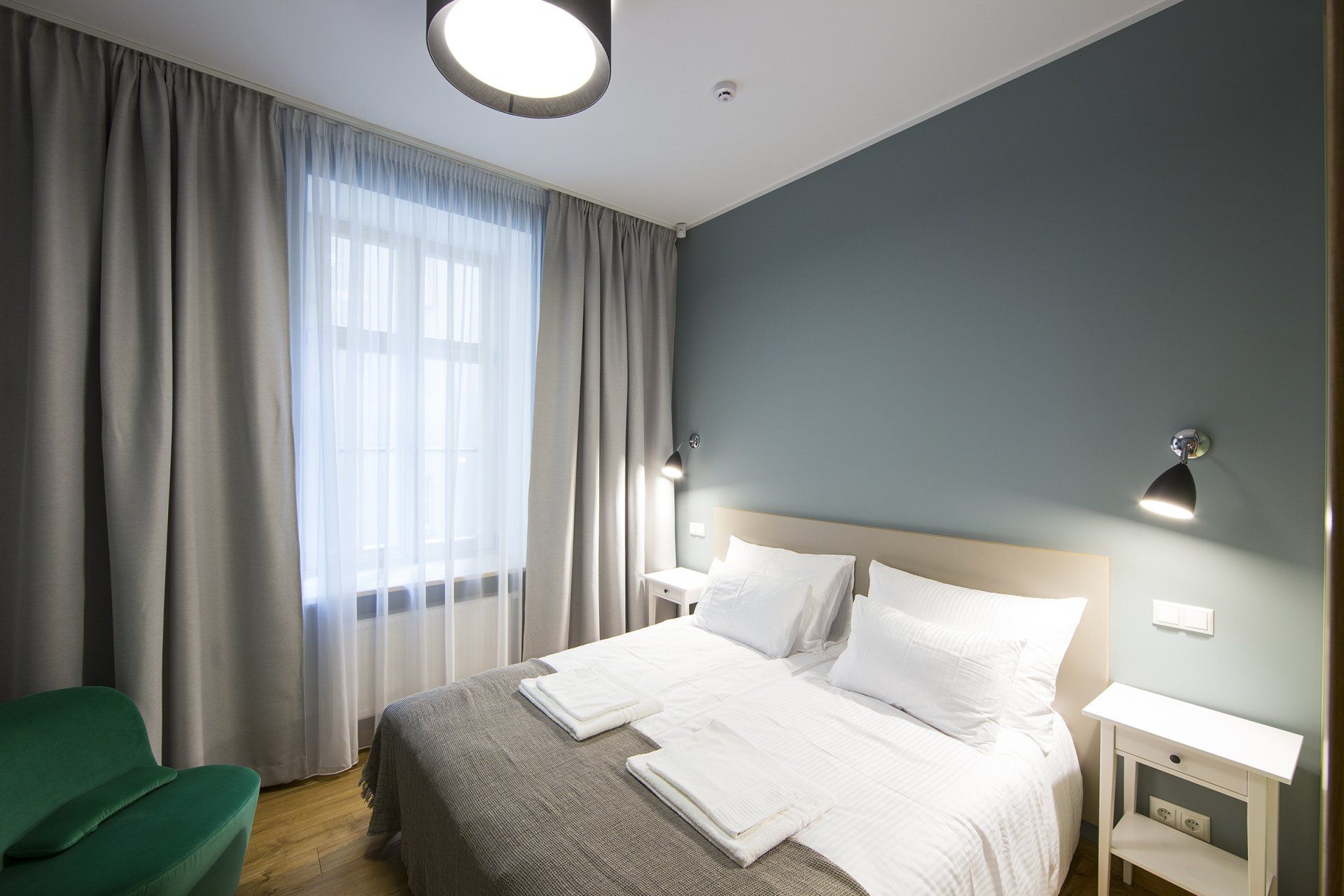 A hotel room with a bed , nightstand , lamp and window.