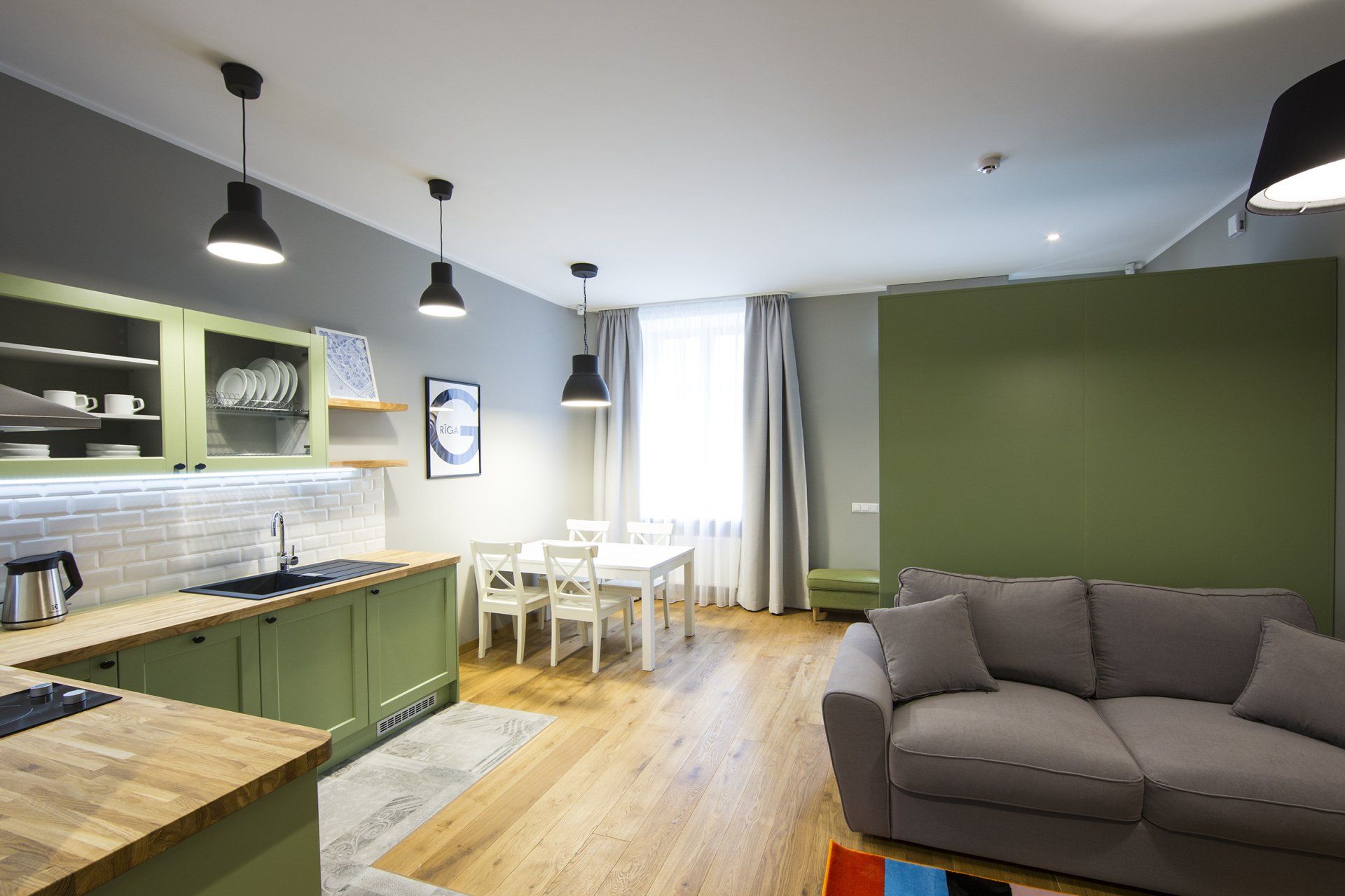 A living room with a couch and a kitchen with green cabinets.