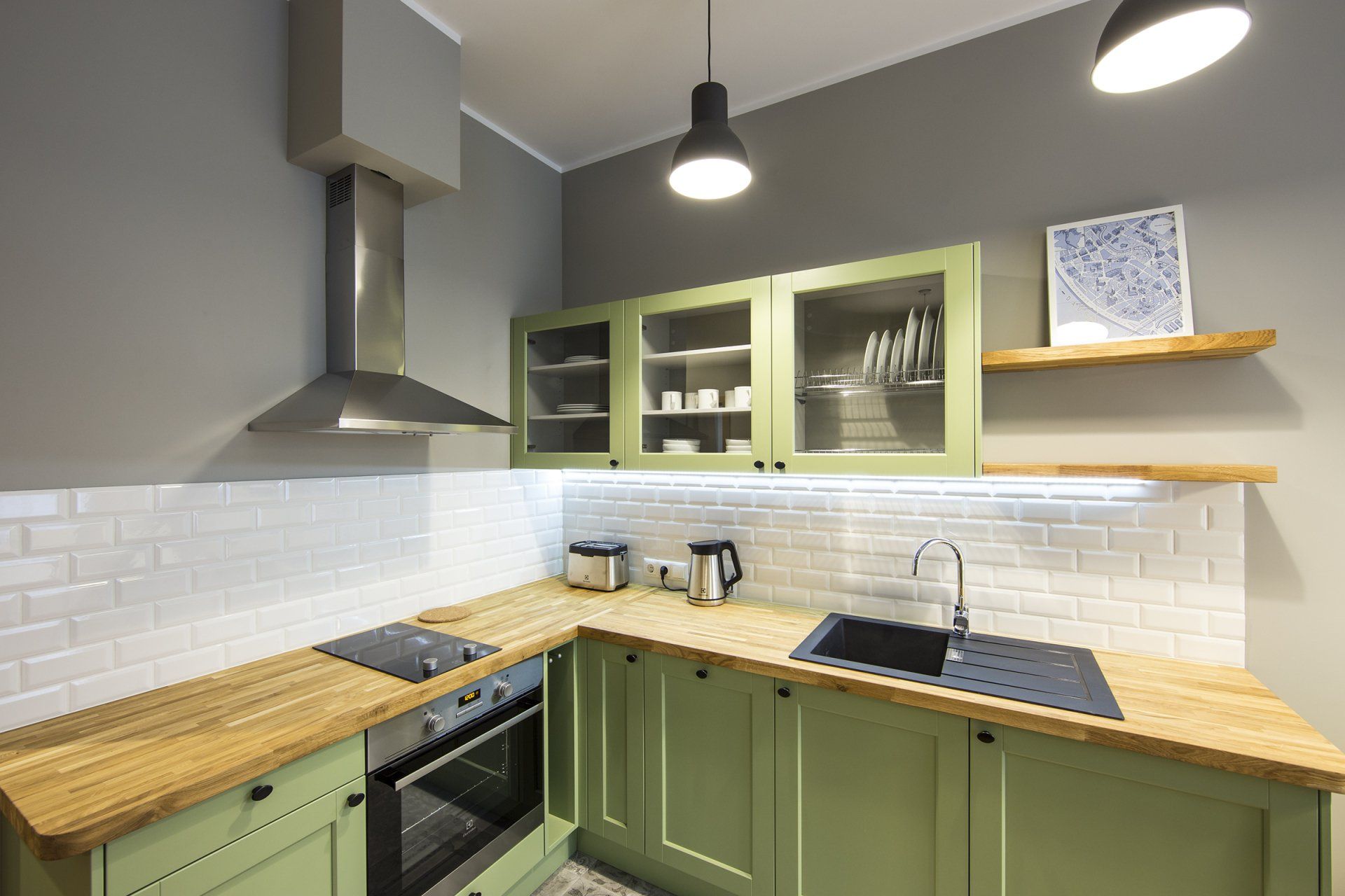 A kitchen with green cabinets , a stove , a sink , and a hood.
