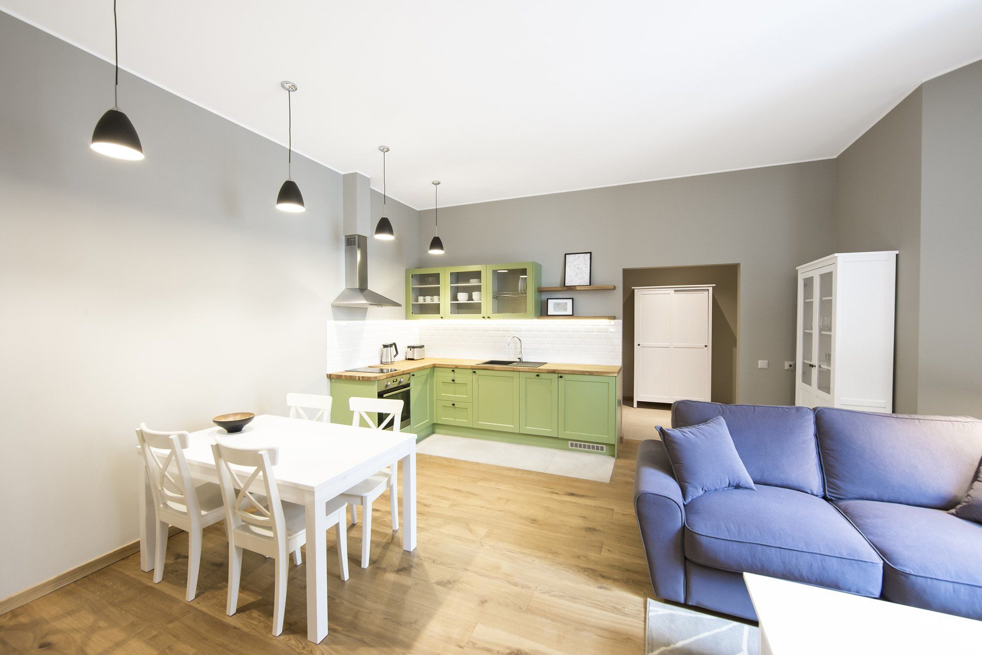 A living room with a blue couch , white table and chairs , and a kitchen.